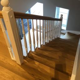 MMK Marcel Pieczka - Drewniane schody z białymi balustradami, widok z góry, naturalne światło z okna w tle.