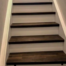 Schody drewniane z ciemnymi stopniami i białymi podstopnicami, widoczne okrągłe zaślepki w stopnicach.