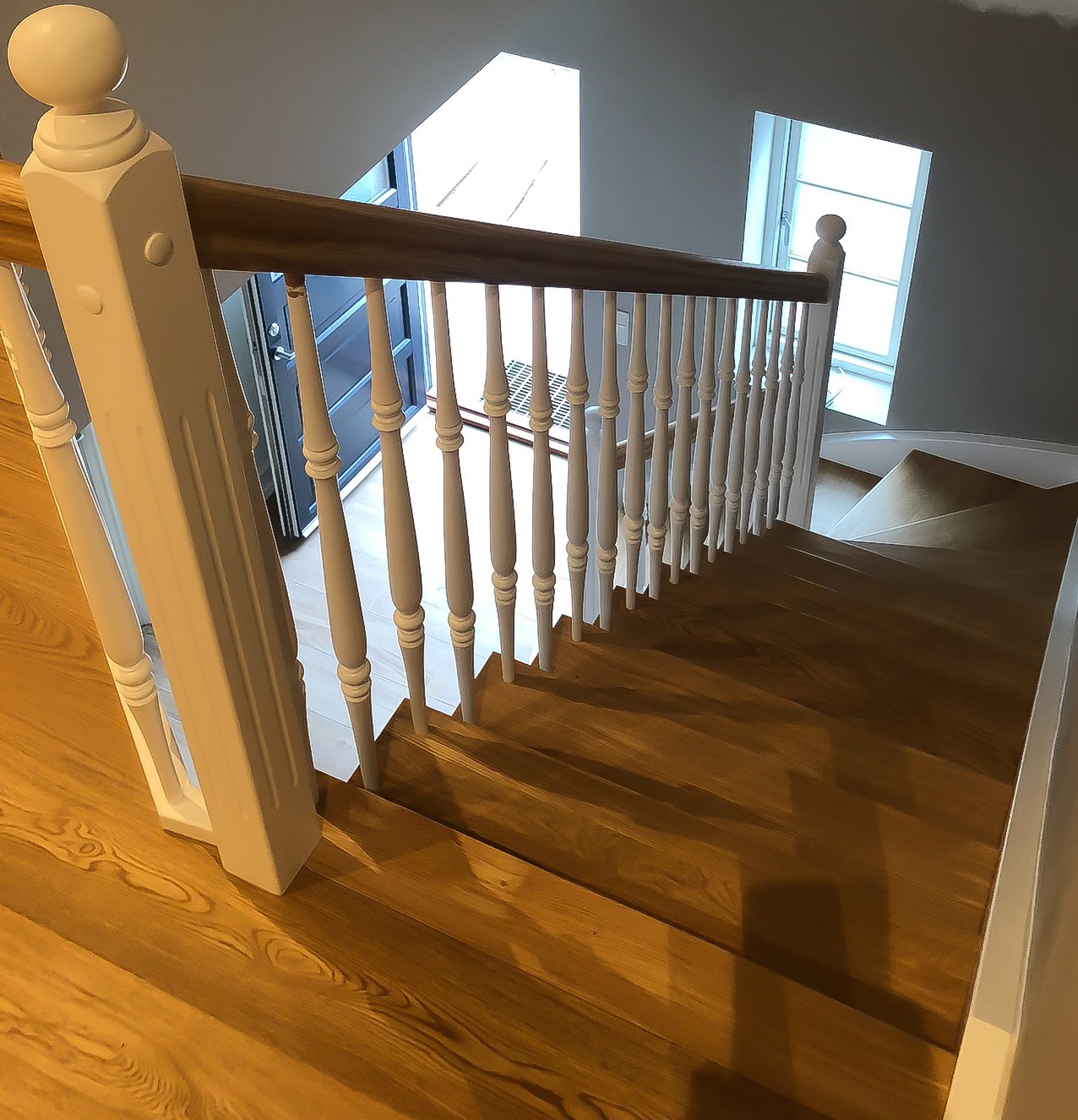 Drewniane schody z białymi balustradami, widok z góry, naturalne światło z okna w tle.