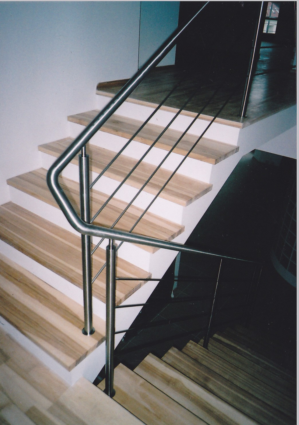 Schody drewniane z białymi podstopnicami i balustradą ze stali nierdzewnej z poziomymi prętami, widok z góry na dół.