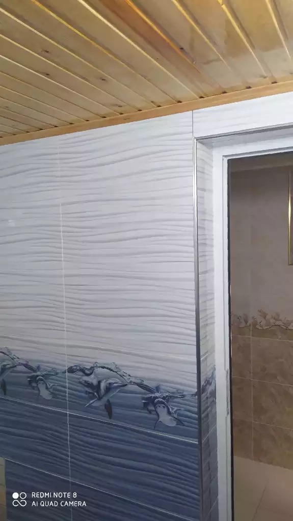 Wykończona łazienka z drewnianym sufitem, biało-niebieskimi płytkami imitującymi fale i motywem delfinów, widoczne drzwi do kabiny prysznicowej.