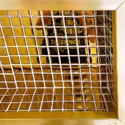Ściana wykończona błyszczącą, złotą mozaiką kwadratową z białymi fugami, ujęcie z bliska, widoczny fragment ramy.