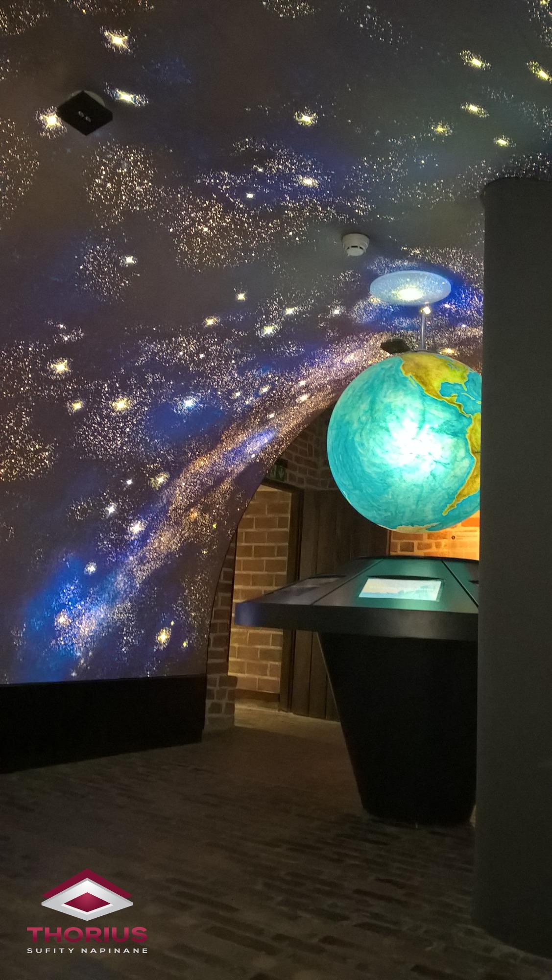 Sufit z efektem rozgwieżdżonego nieba, z widocznym globusem i elementami ceglanej ściany w tle, oświetlenie punktowe.