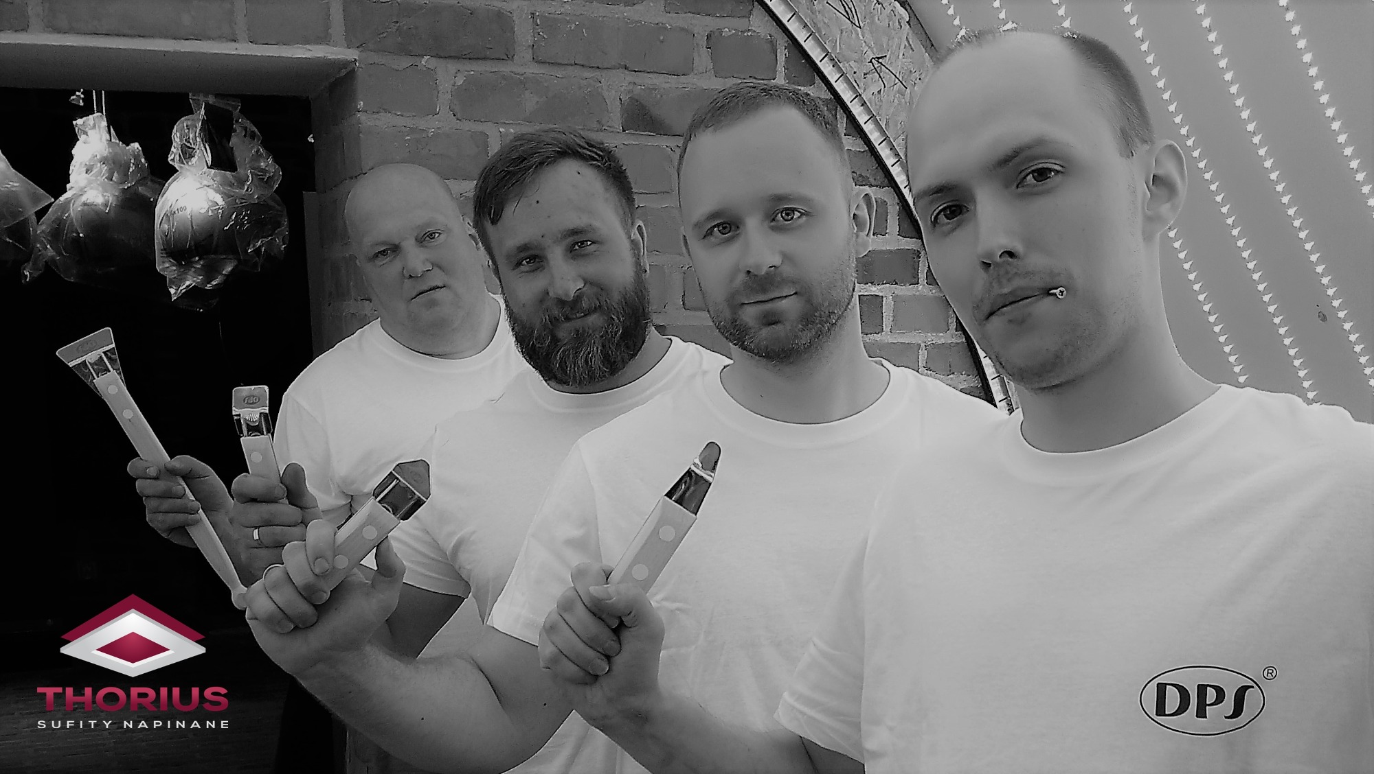 Czterech mężczyzn w białych koszulkach trzyma narzędzia do montażu sufitów napinanych, z logo firmy Thorius w lewym dolnym rogu i DPS na koszulce jednego z mężczyzn.