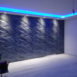 Nowoczesna ściana z panelami 3D w kolorze grafitowym, podświetlona listwą LED w kolorze niebieskim, widok na fragment okna i rośliny doniczkowe, jasna podłoga.