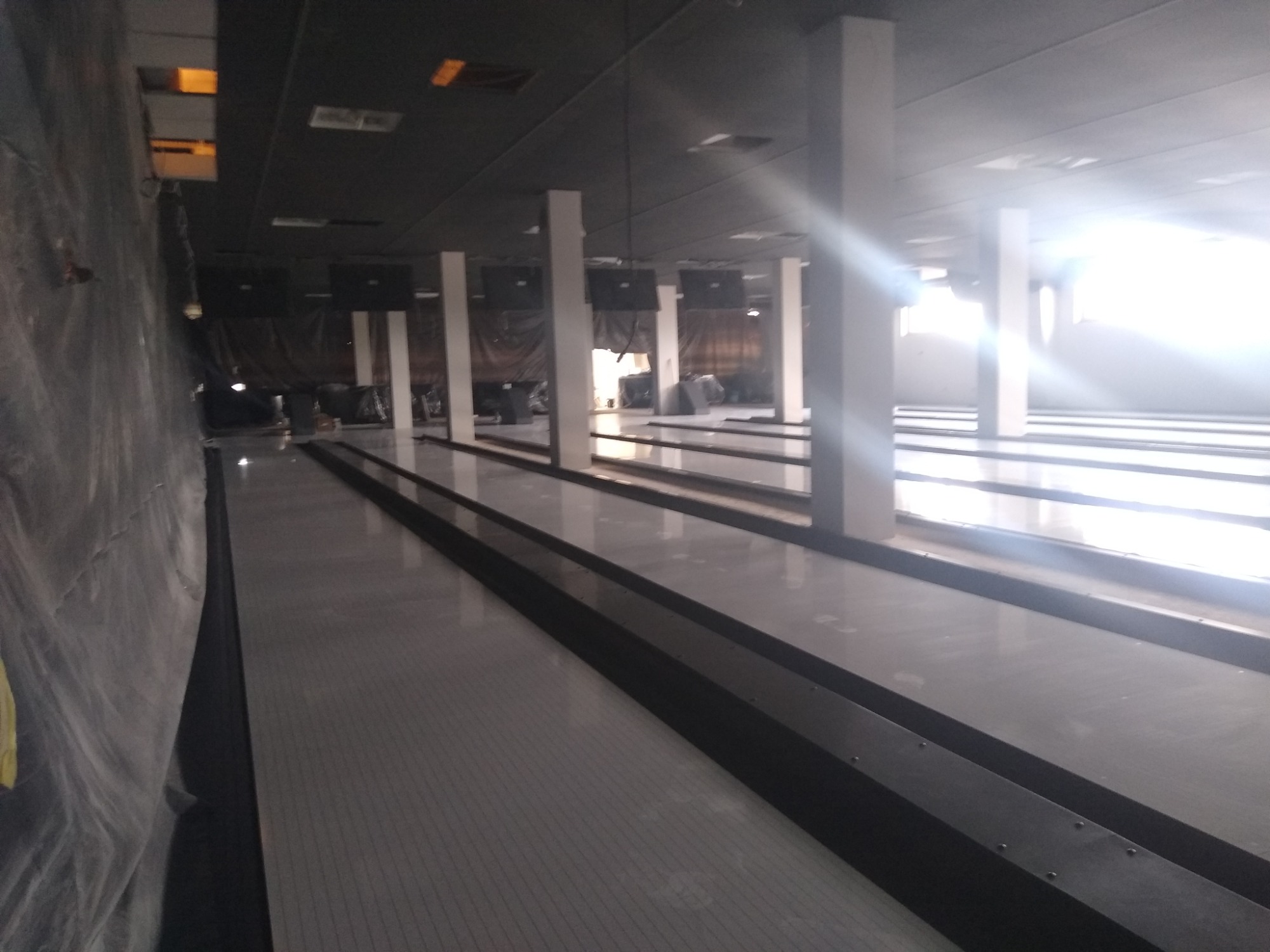 Wnętrze remontowanego lokalu z przygotowanymi torami do gry w kręgle, zabezpieczonymi folią ścianami i surowym oświetleniem.