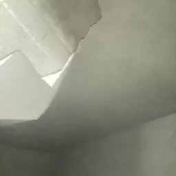 Niedokończona gładź na suficie i ścianie, widoczne nierówności i fragmenty starej powierzchni, oświetlenie od góry podkreśla niedoskonałości.