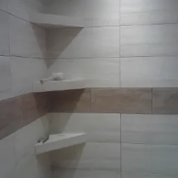 Wykończona łazienka z beżowymi płytkami imitującymi drewno, z wnęką i półkami, na których leżą akcesoria łazienkowe.