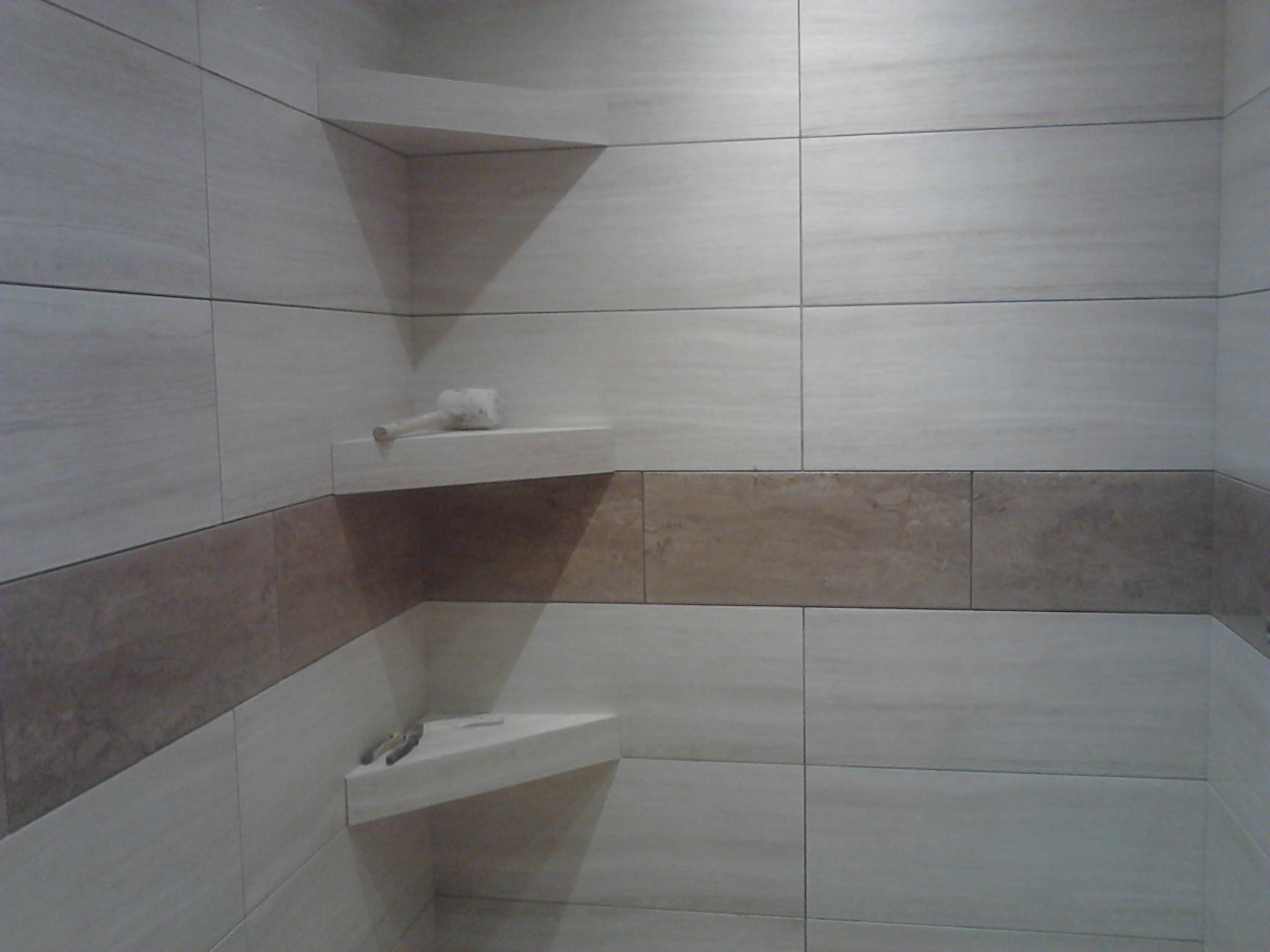 Wykończona łazienka z beżowymi płytkami imitującymi drewno, z wnęką i półkami, na których leżą akcesoria łazienkowe.