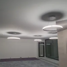 Wnętrze pomieszczenia z zamontowanymi, nowoczesnymi, okrągłymi lampami LED pod sufitem, widoczne ślady prac wykończeniowych na podłodze.