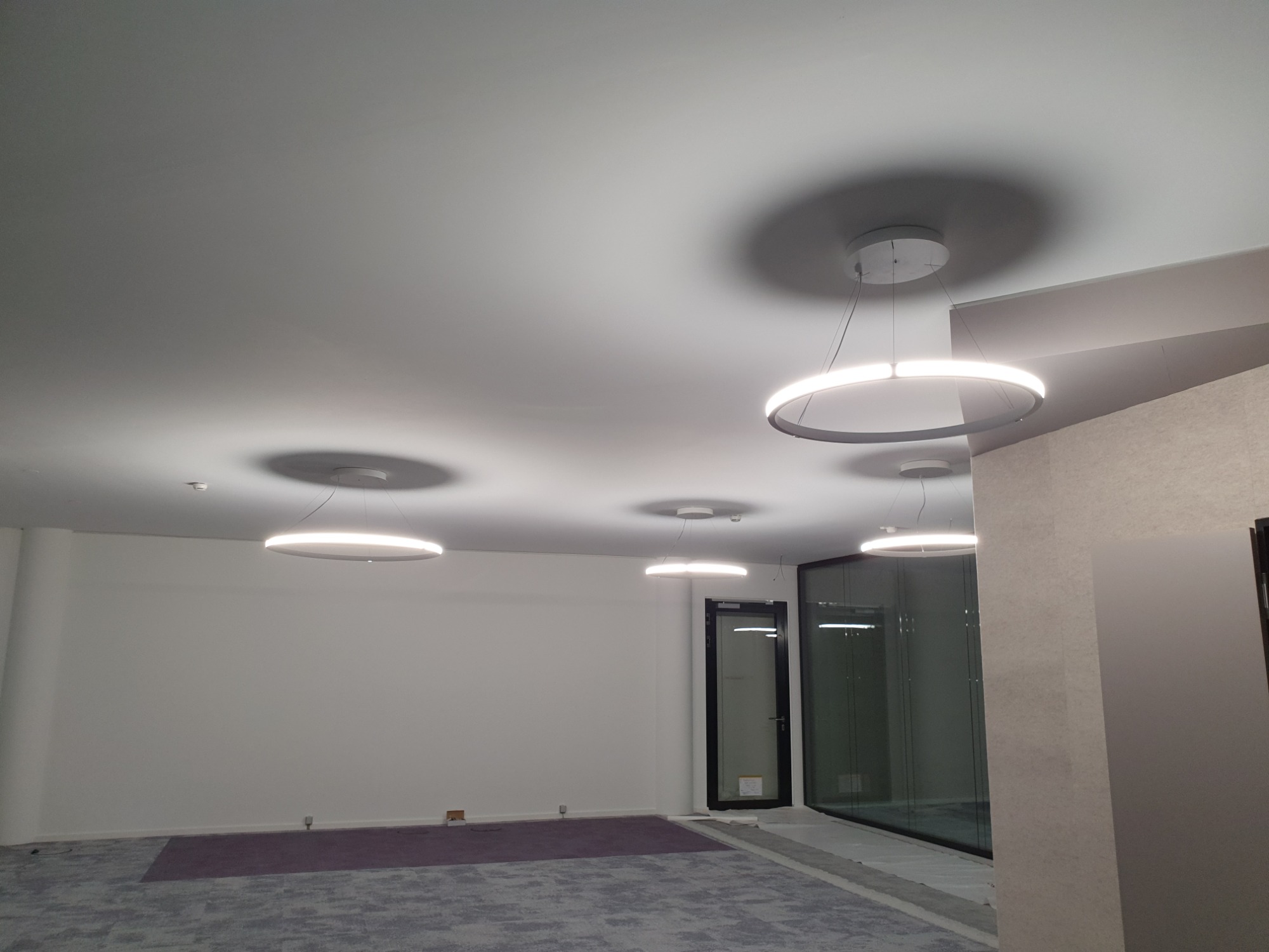 Wnętrze pomieszczenia z zamontowanymi, nowoczesnymi, okrągłymi lampami LED pod sufitem, widoczne ślady prac wykończeniowych na podłodze.