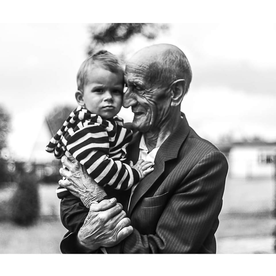 Czarno-białe zdjęcie starszego mężczyzny w garniturze, trzymającego na rękach małe dziecko w bluzie w paski; obaj patrzą w obiektyw.