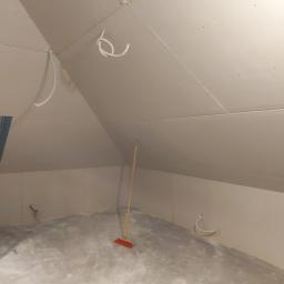 NEW HOUSE - Poddasze w trakcie prac wykończeniowych: zamontowane płyty gipsowo-kartonowe na ścianach i skosach, widoczne wystające kable, drabina oparta o ścianę przy oknie dachowym, na podłodze leży miotła.