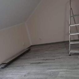 NEW HOUSE - Poddasze po malowaniu ścian na jasny odcień, z widocznym oknem dachowym, grzejnikiem, drabiną i wałkiem do malowania na podłodze z paneli.