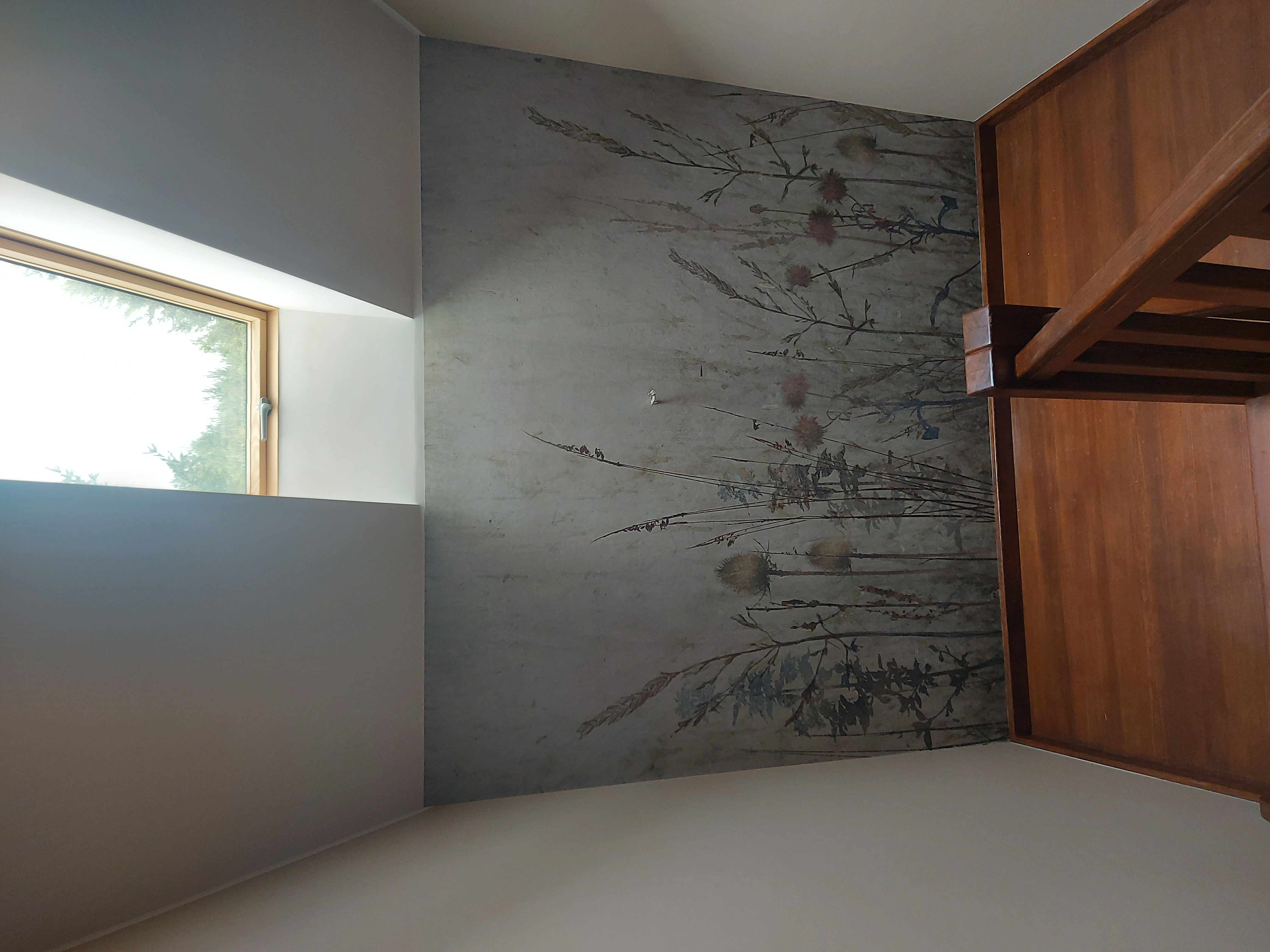 Ściana w pokoju na poddaszu z motywem roślinnym, drewniane schody i okno dachowe w białej ramie.