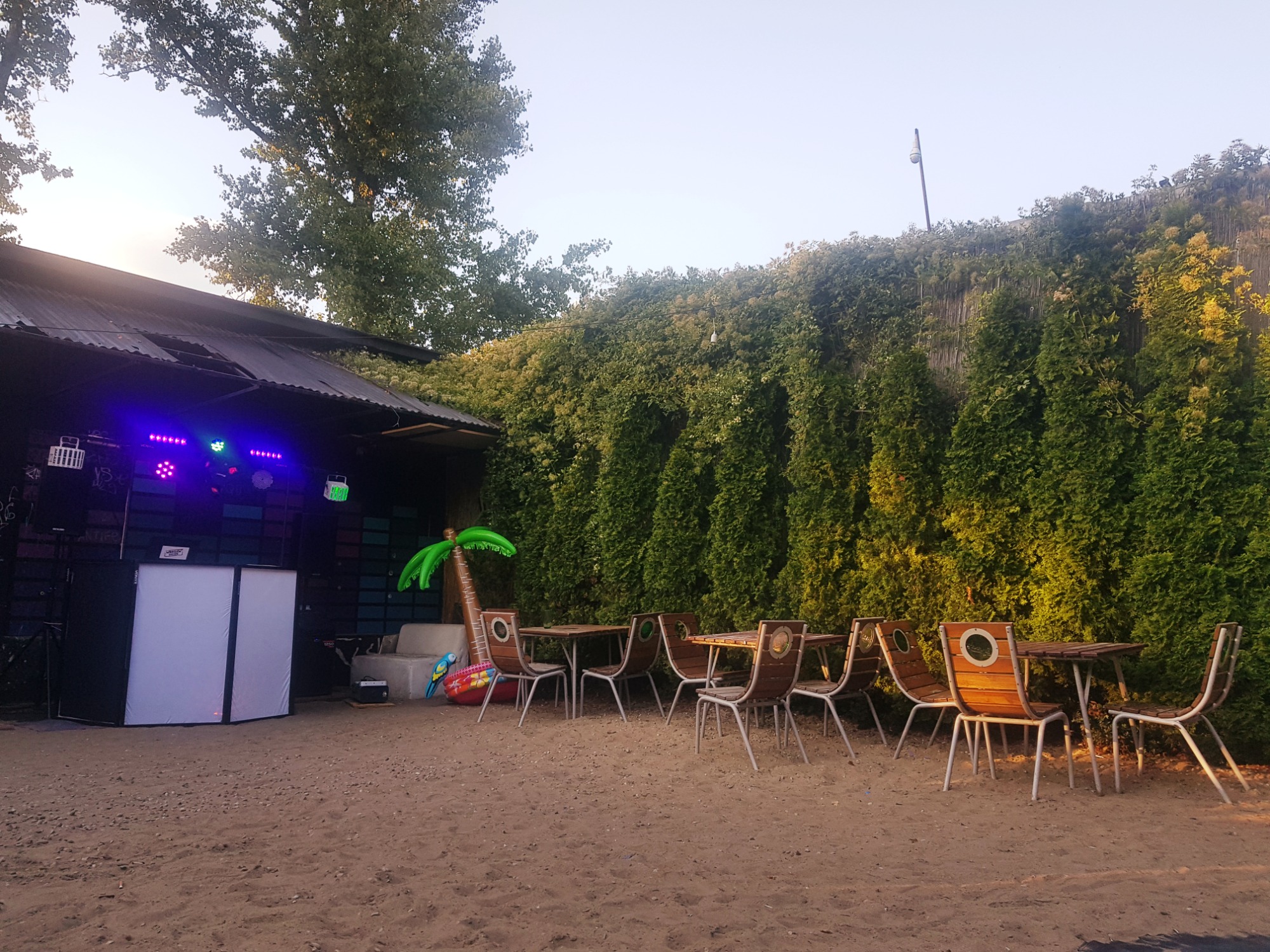 Scena z nagłośnieniem i oświetleniem na zewnątrz, stoliki z krzesłami, dekoracje w postaci dmuchanej palmy i koła ratunkowego, piasek na podłożu.