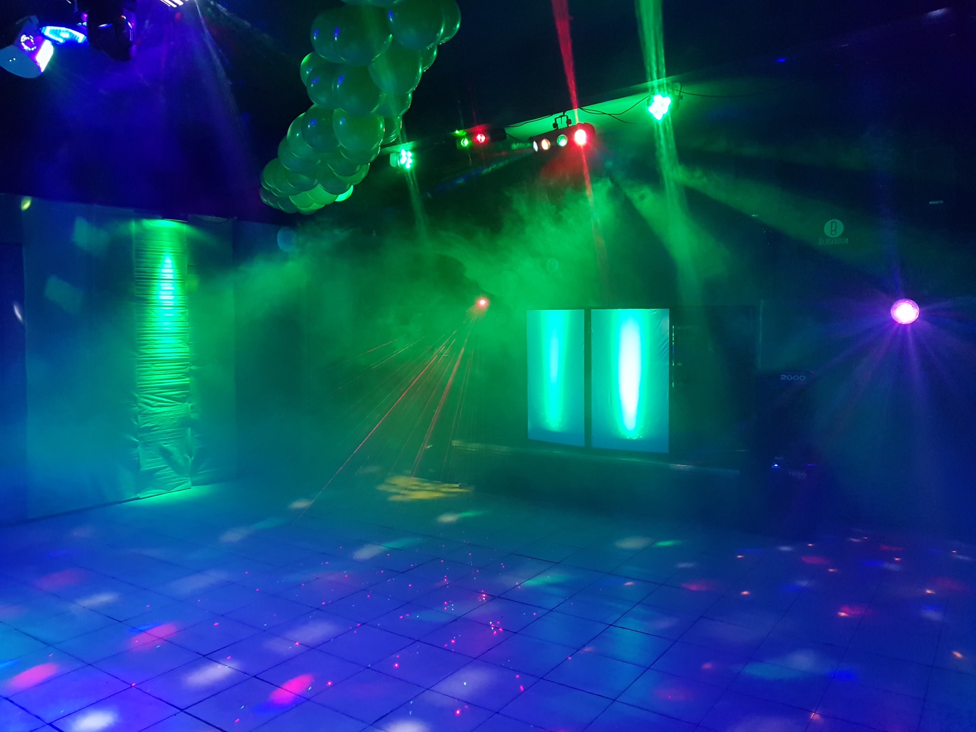 Pusta sala taneczna z podświetlanym parkietem, zielonymi balonami pod sufitem, dwoma pionowymi panelami LED i efektem mgły