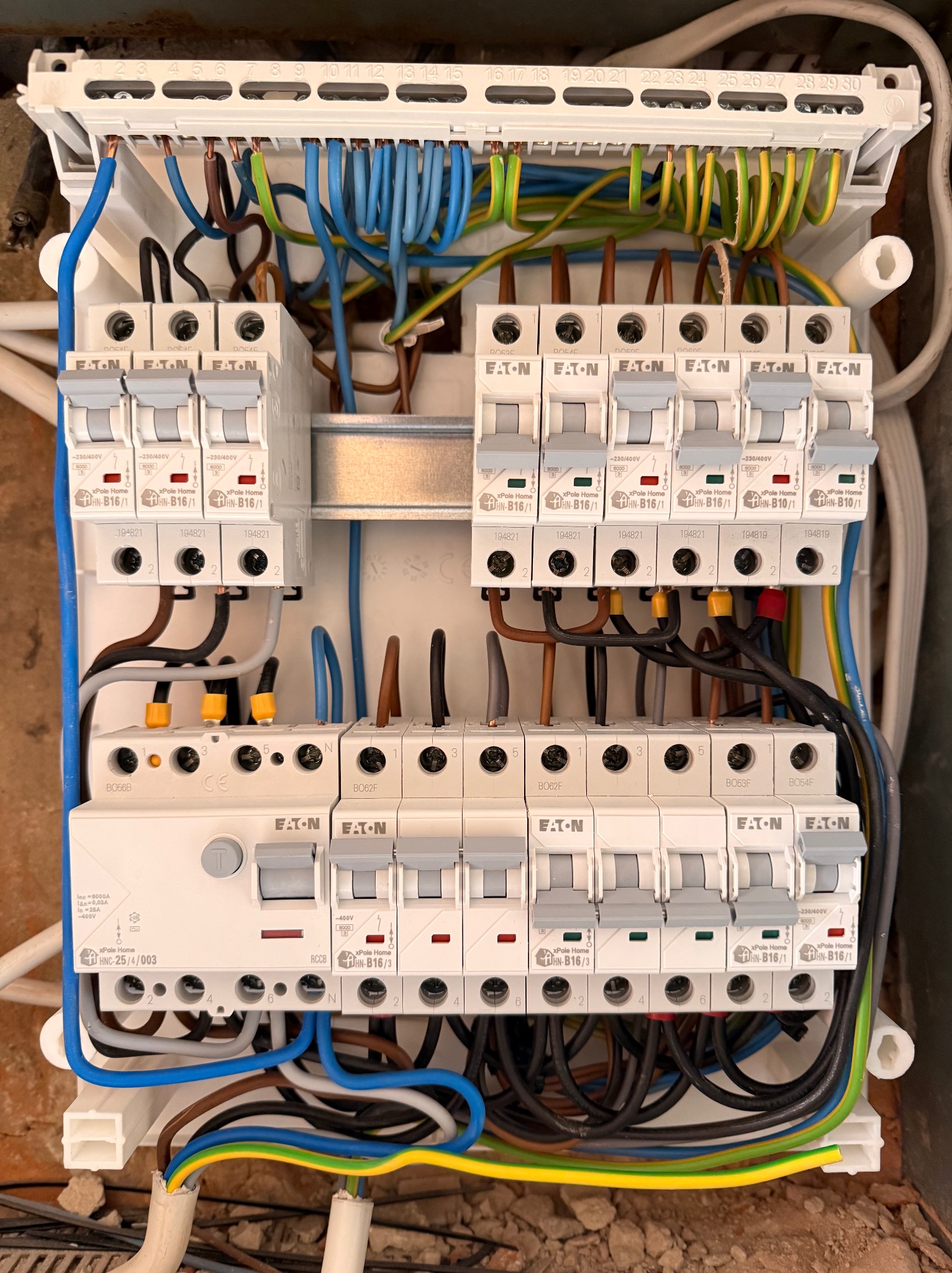 Otwarta skrzynka bezpiecznikowa z widocznymi bezpiecznikami Eaton, różnokolorowymi przewodami i numeracją. Instalacja w trakcie prac, widoczne detale połączeń.