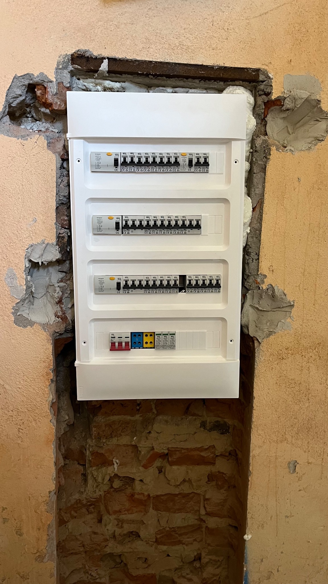 Nowa, biała skrzynka rozdzielcza zamontowana we wnęce w ścianie, widoczne uszczelnienia pianką montażową i świeże tynki.
