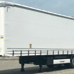 Biała naczepa Krone z plandeką na parkingu, widok z boku, tabliczka ostrzegawcza ADR. Naczepa do nauki jazdy kat. C+E.