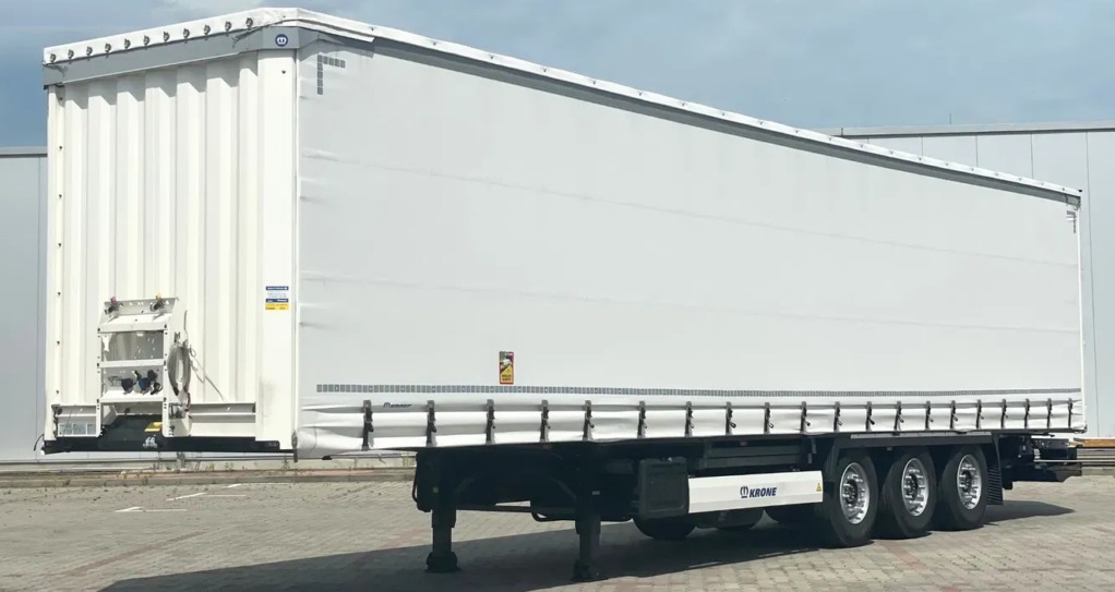 Biała naczepa Krone z plandeką na parkingu, widok z boku, tabliczka ostrzegawcza ADR. Naczepa do nauki jazdy kat. C+E.