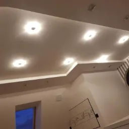 Podwieszany sufit z oświetleniem punktowym i listwą LED, widok z dołu, ściana z tapetą w pionowe pasy w tle.