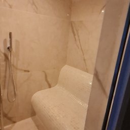 Mateusz Świeczkowski - Wnętrze sauny z siedziskiem wyłożonym mozaiką, marmurowe ściany i podłoga, widoczny prysznic i oświetlenie punktowe.