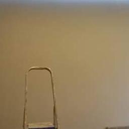 Mateusz Świeczkowski - Świeżo pomalowana ściana w odcieniach beżu z drabiną i drzwiami w folii, przygotowanymi do montażu.