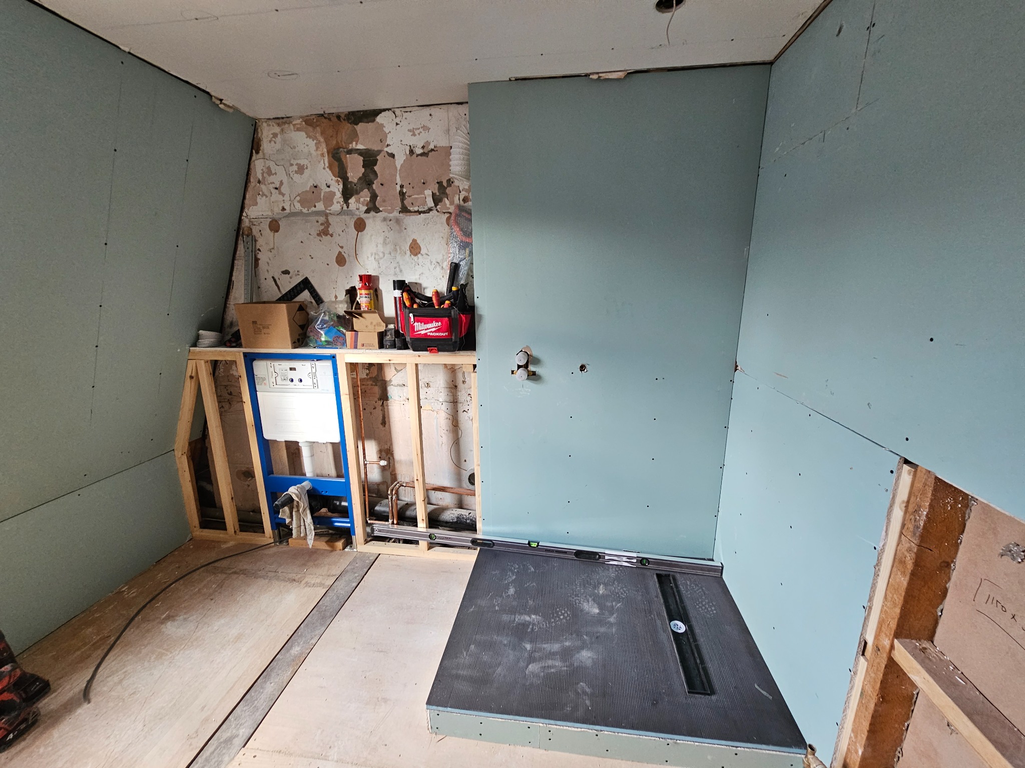 Łazienka w trakcie remontu: montaż stelaża podtynkowego WC na drewnianej konstrukcji, przygotowanie podłoża pod prysznic z odpływem liniowym, ściany wykończone płytami gipsowo-kartonowymi w kolorze...