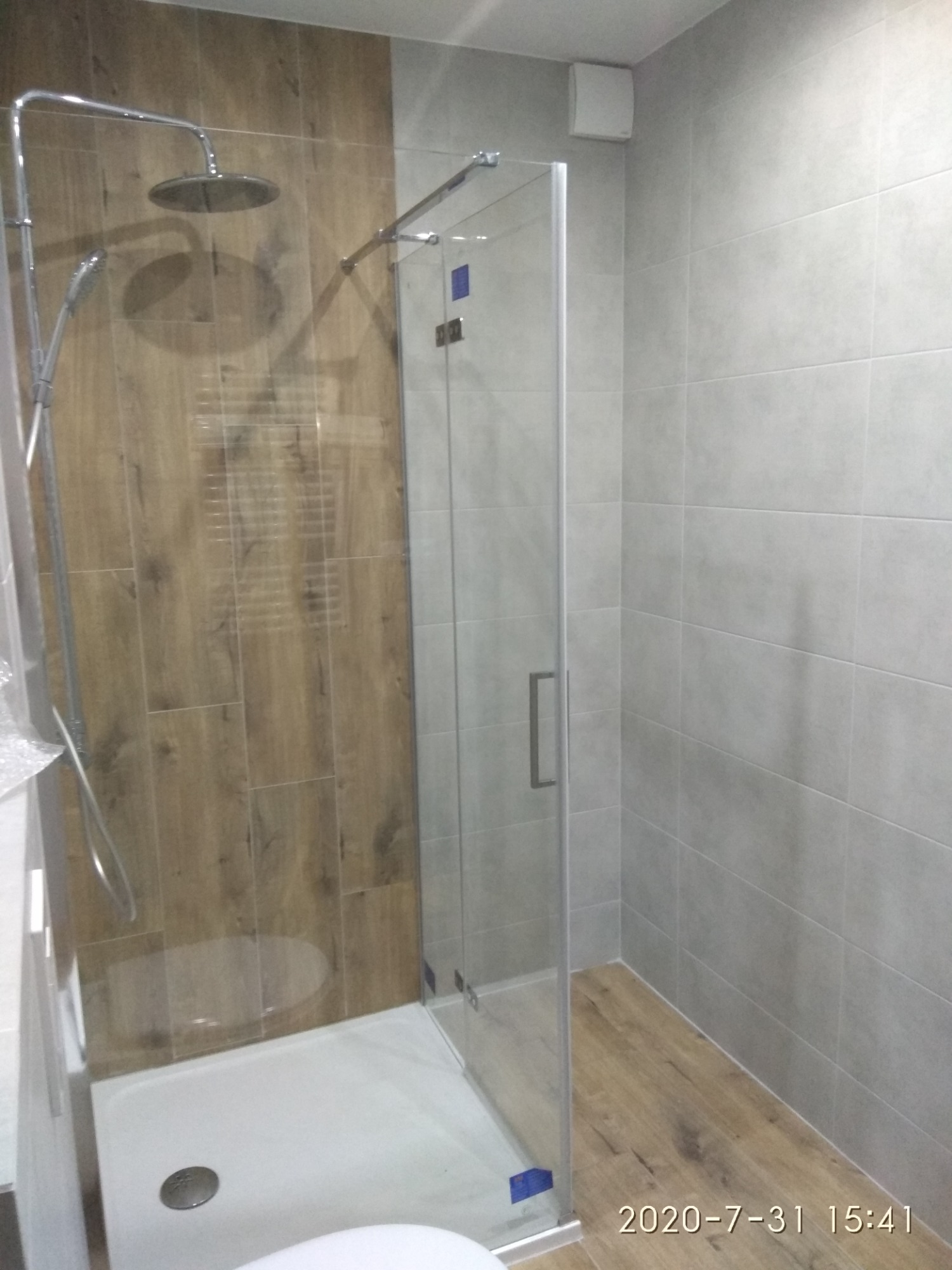 Wykończona łazienka z kabiną prysznicową typu walk-in, drewnopodobne płytki na ścianie prysznica i podłodze, szare płytki na pozostałych ścianach, widoczny odpływ liniowy.