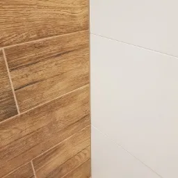 Połączenie płytek drewnopodobnych ułożonych pod kątem z białymi, błyszczącymi płytkami ściennymi z delikatnymi wgłębieniami.