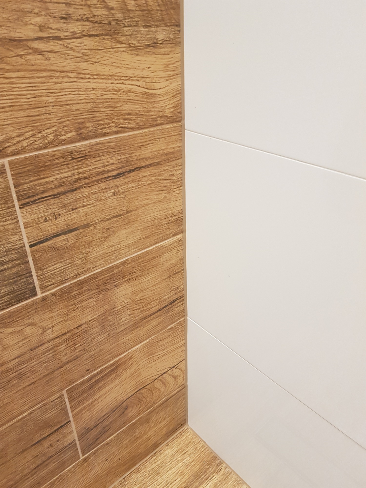 Połączenie płytek drewnopodobnych ułożonych pod kątem z białymi, błyszczącymi płytkami ściennymi z delikatnymi wgłębieniami.