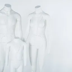 Trzy białe, minimalistyczne manekiny: męski, damski i dziecięcy, z zaznaczonymi liniami kroju, ustawione na białym tle.