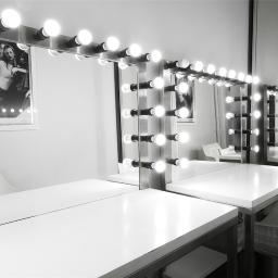 IN2IT Studio - Czarno-białe zdjęcie pustej garderoby z lustrami otoczonymi żarówkami, białe blaty i designerskie krzesła, na ścianie plakat z modelką.