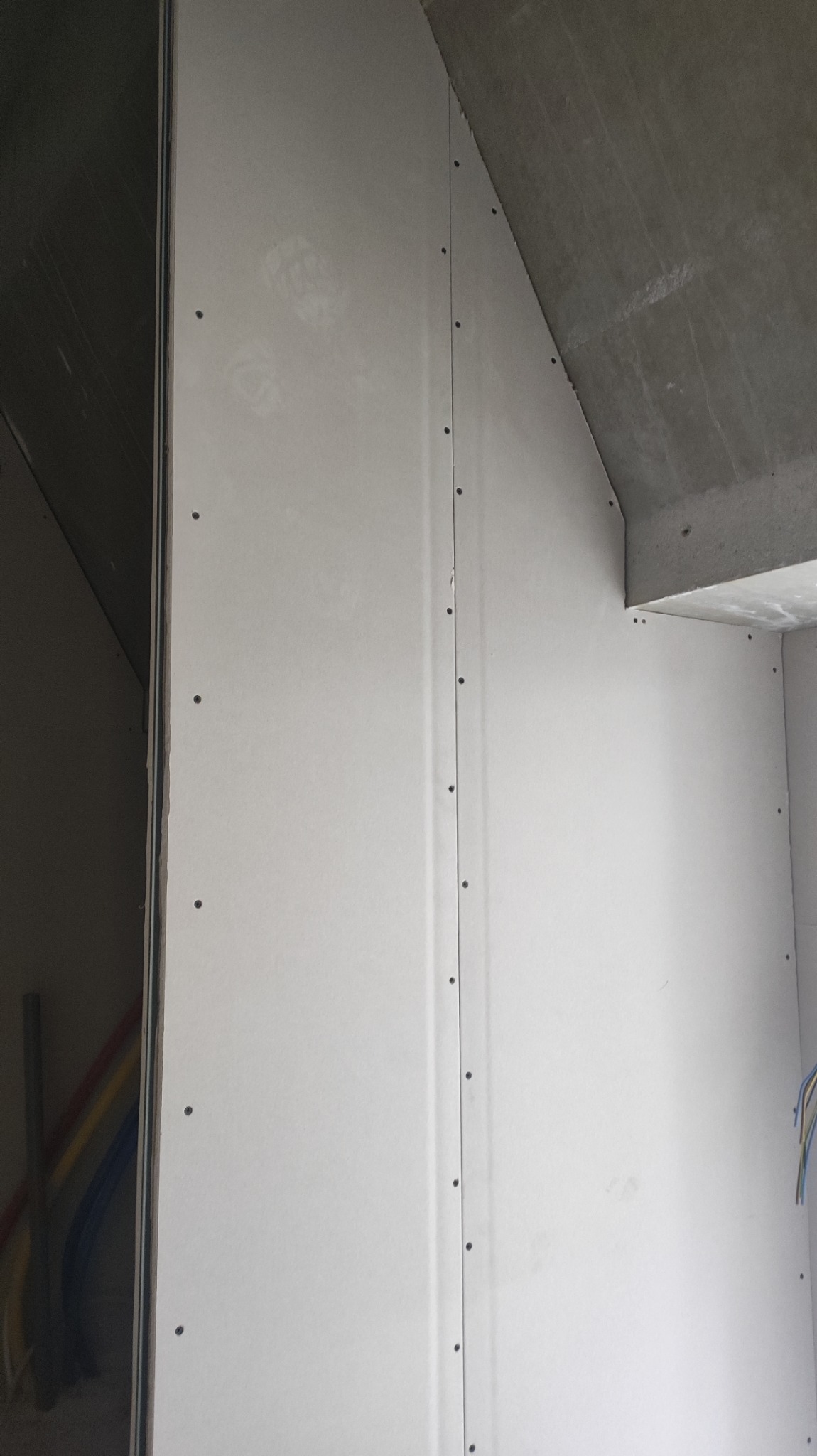 Ściana z płyt kartonowo-gipsowych zamontowana na metalowym stelażu, widoczne wkręty mocujące, surowy betonowy strop w tle.