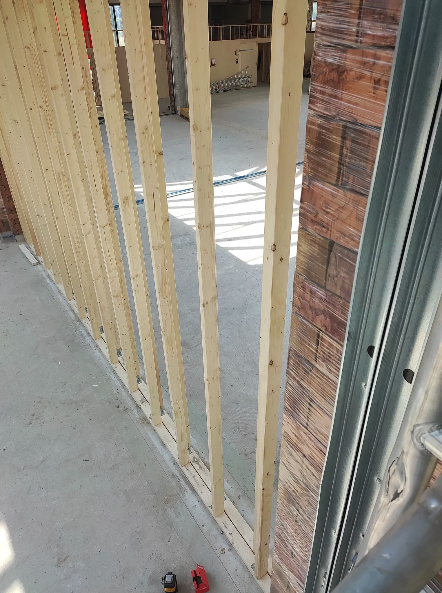 Wznoszenie szkieletu ściany działowej z drewnianych belek, widoczne narzędzia pomiarowe na podłodze, w tle surowy stan pomieszczenia.
