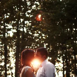 Para młoda obejmująca się na tle drzew, z promieniami słońca przebijającymi się między nimi, tworząc efektowną aureolę.