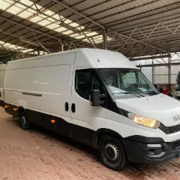 Biały samochód dostawczy Iveco na ceglanym podłożu w hali z metalową konstrukcją dachu, obok wózek widłowy.