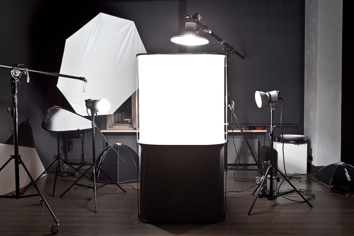 Studio fotograficzne z licznymi lampami, softboxami i tłem, przygotowane do sesji zdjęciowej na ciemnym tle i drewnianej podłodze.