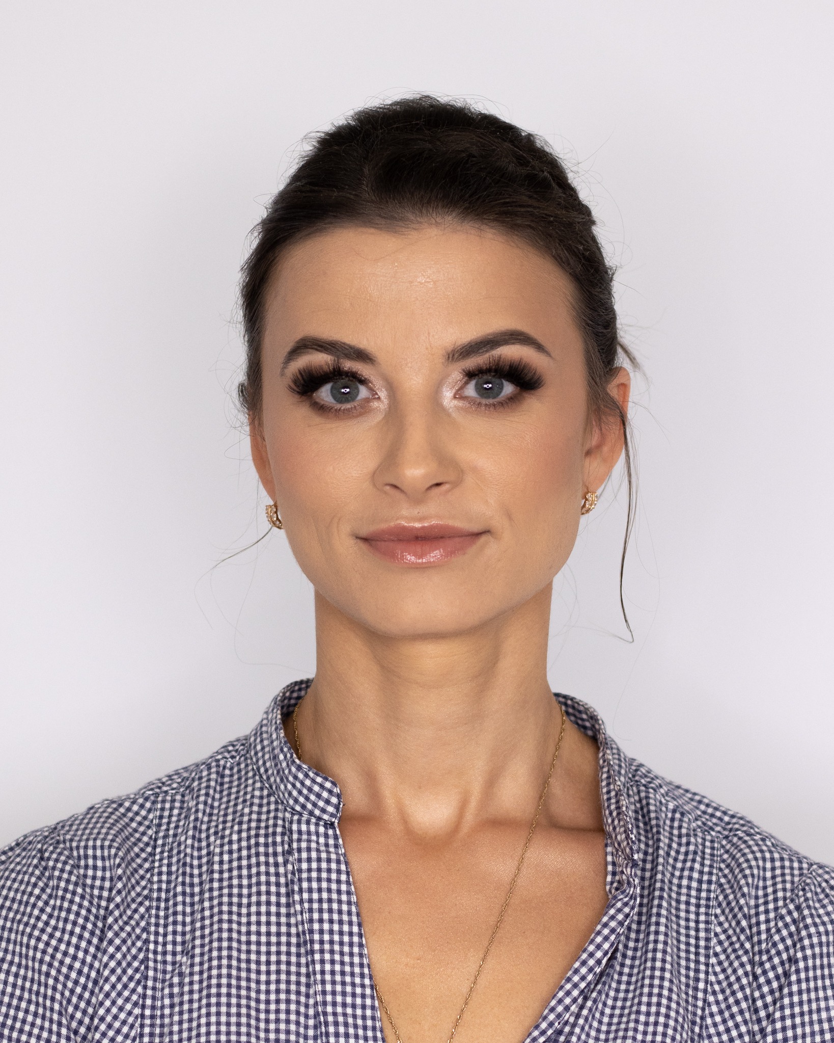 Portret kobiety z profesjonalnie wykonanym dziennym wizażem, podkreślone rzęsy i błyszczące usta, delikatna biżuteria, na białym tle.