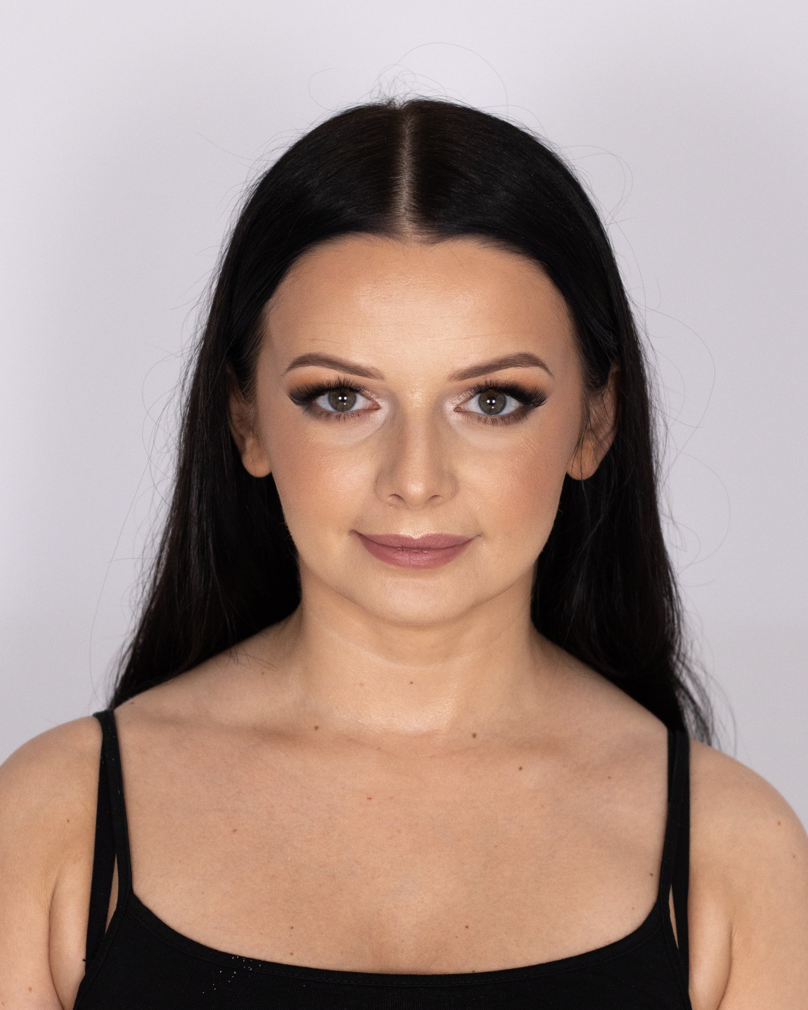 Portret kobiety z delikatnym, dziennym upiększeniem oczu i ust, podkreślonymi brwiami i długimi, czarnymi włosami na jasnym tle.