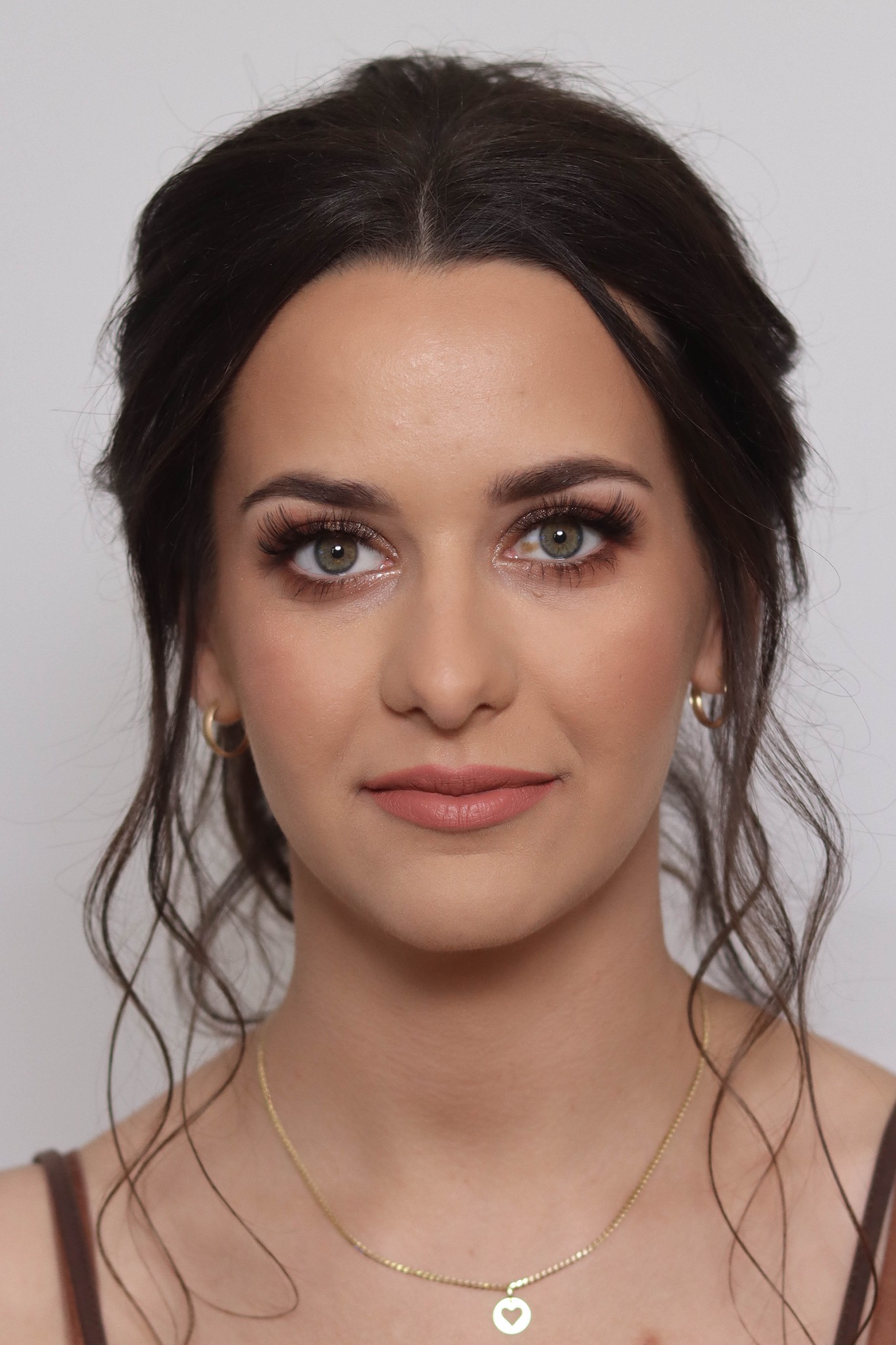 Portret kobiety z delikatnym, dziennym upiększeniem, podkreślonymi rzęsami i subtelnym różem na policzkach, noszącej złotą biżuterię.
