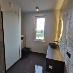 Nowoczesna łazienka z kabiną prysznicową typu walk-in, umywalką nablatową i podświetlanym lustrem. Grafitowa armatura i marmurowe wykończenie ścian.