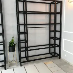 Metalowa konstrukcja regału z drążkiem na ubrania i półkami w Nadarzynie, przygotowana do montażu z widocznymi białymi elementami obudowy u dołu.