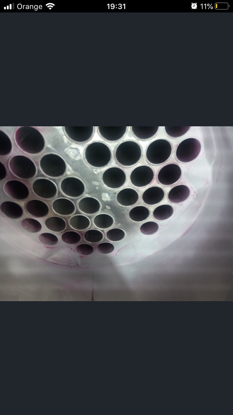 Zbliżenie na wiązkę rur ze stali nierdzewnej podczas testu szczelności barwnikowego, widoczne ślady penetrantu w kolorze różowym.