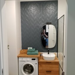 E i J JAROSŁAW KĘDZIORA REMONTY I WYKOŃCZENIA WNĘTRZ - Nowoczesna łazienka z szarą ścianą z płytek ułożonych w jodełkę, drewnianym blatem z umywalką nablatową, pralką Electrolux i lustrem owalnym, odbicie fotografa.