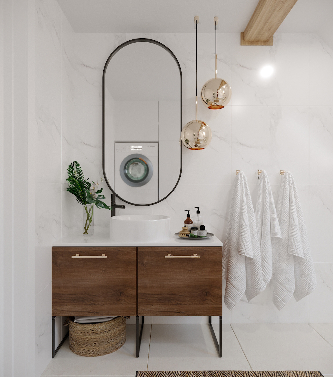 Nowoczesna łazienka z umywalką nablatową, szafką z drewnianym fornirem i owalnym lustrem z czarną ramą, w której odbija się pralka; złote lampy wiszące i białe ręczniki na tle marmurowych płytek.