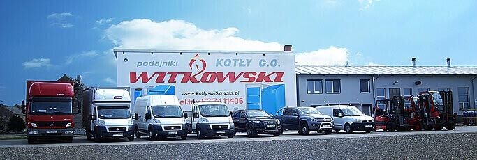 Flota pojazdów firmy Witkowski Kotły C.O. zaparkowana przed budynkiem z dużym szyldem reklamowym prezentującym logo i nazwę firmy.