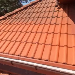 Częściowo wyczyszczony dach z czerwonej dachówki karpiówki, widoczna różnica między czystą a zabrudzoną powierzchnią, rynna wzdłuż krawędzi dachu.