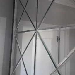 Dekoracyjna ściana z lustrzanych rombów, widoczne odbicie białych drzwi z klamką i zawiasami.